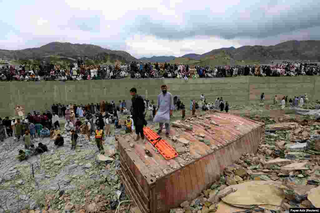 Rescue workers and onlookers stand around a damaged supply vehicle.