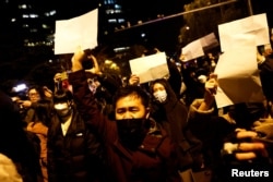 People gather for a vigil and hold white sheets of paper in protest of COVID-19 restrictions as they commemorate the victims of a fire in Urumqi in Beijing on November 27.