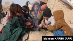 Internally displaced Afghan children warm up around a fire outside their temporary mud house on the outskirts of Herat on December 6.