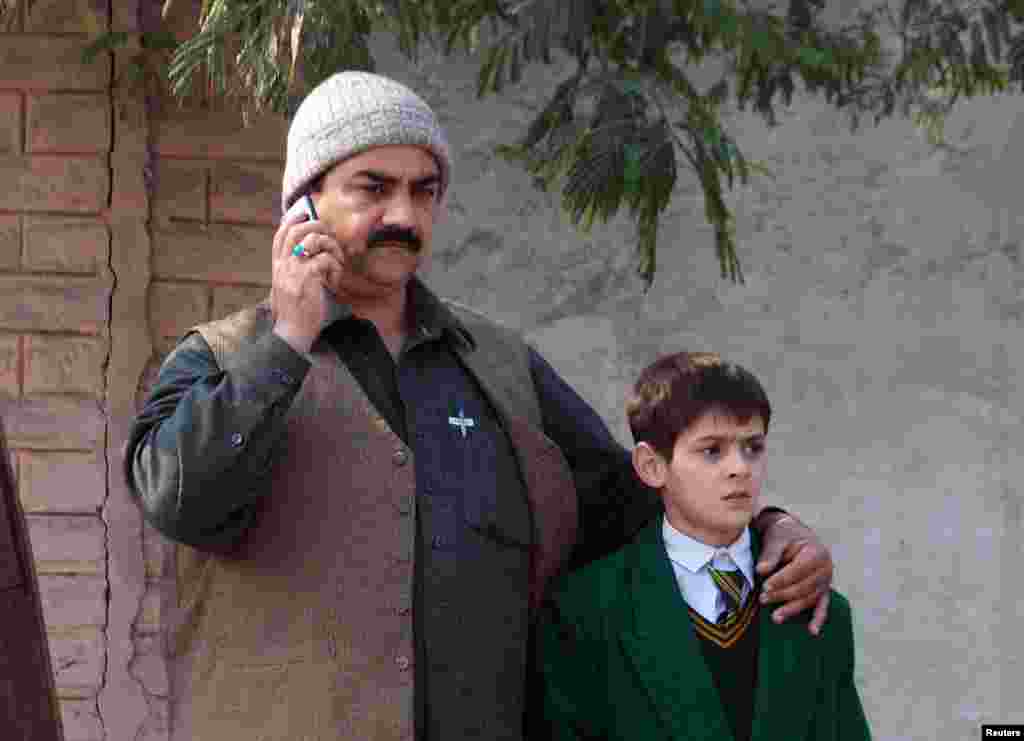 A man talks on a phone while comforting a student outside the military school.