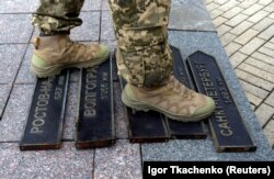 Украинский военнослужащий стоит на табличках с названиями городов России (Ростов-на-Дону, Волгоград, Таганрог, Москва и Санкт-Петербург) после того, как они были демонтированы с декоративного уличного знака в Одессе, что указывает направления и расстояния до ряда городов. Одесса, 14 апреля 2022 года