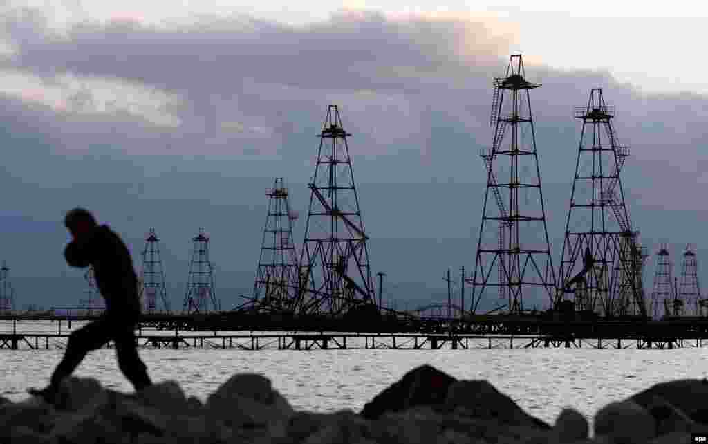 A worker walks in front of the oil derricks on the Caspian Sea near Baku. With no end in sight to the economic crisis President Aliyev has made a plea for citizens to &quot;work more efficiently.&quot; But patience on the street for the big-spending regime is wearing thin.&nbsp;