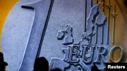 People are silhouetted in front of a large euro coin during a ceremony in Frankfurt in December.