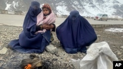 Gulnaz (left) keeps her 18-month-old son warm as they wait for alms along a highway in eastern Afghanistan.