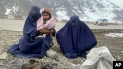 Gulnaz (left) tries to keep her 18-month-old son warm as they wait for alms next to the Kabul-Pul-e Alam highway in eastern Afghanistan.