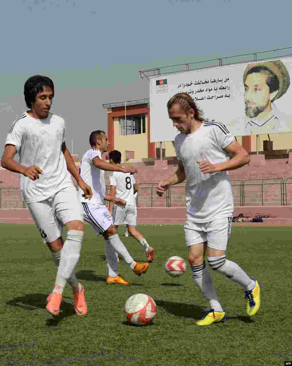 Afghan football players training in Kabul with a poster of legendary Afghan commander Ahmad Shah Masud in the background.